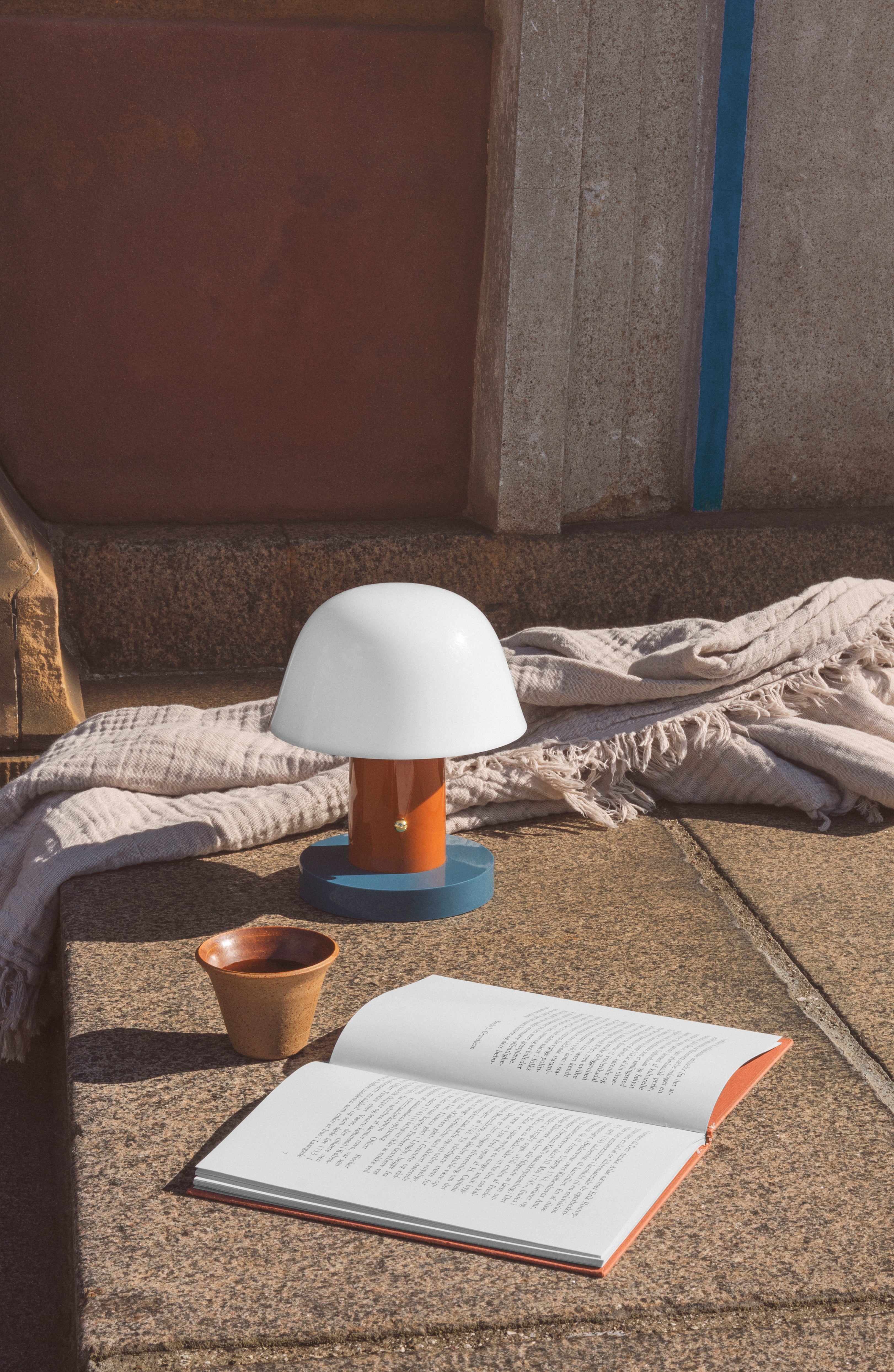 Tragbare Lampe SETAGO JH27 mit cremefarbenem Schirm und orange-blauem Fuß.