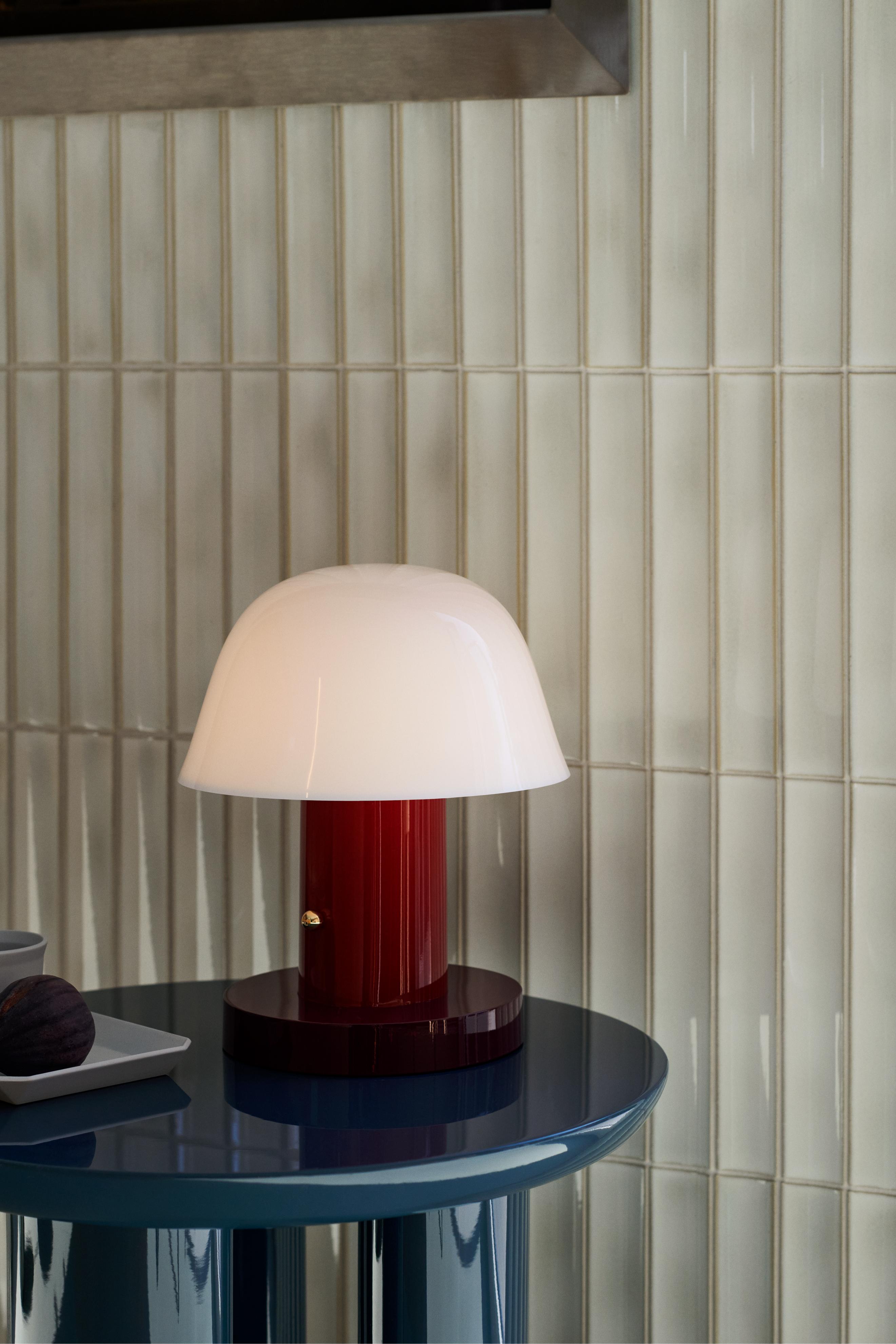 Tragbare Lampe SETAGO JH27 mit cremefarbenem Schirm und dunkelrotem Fuß.