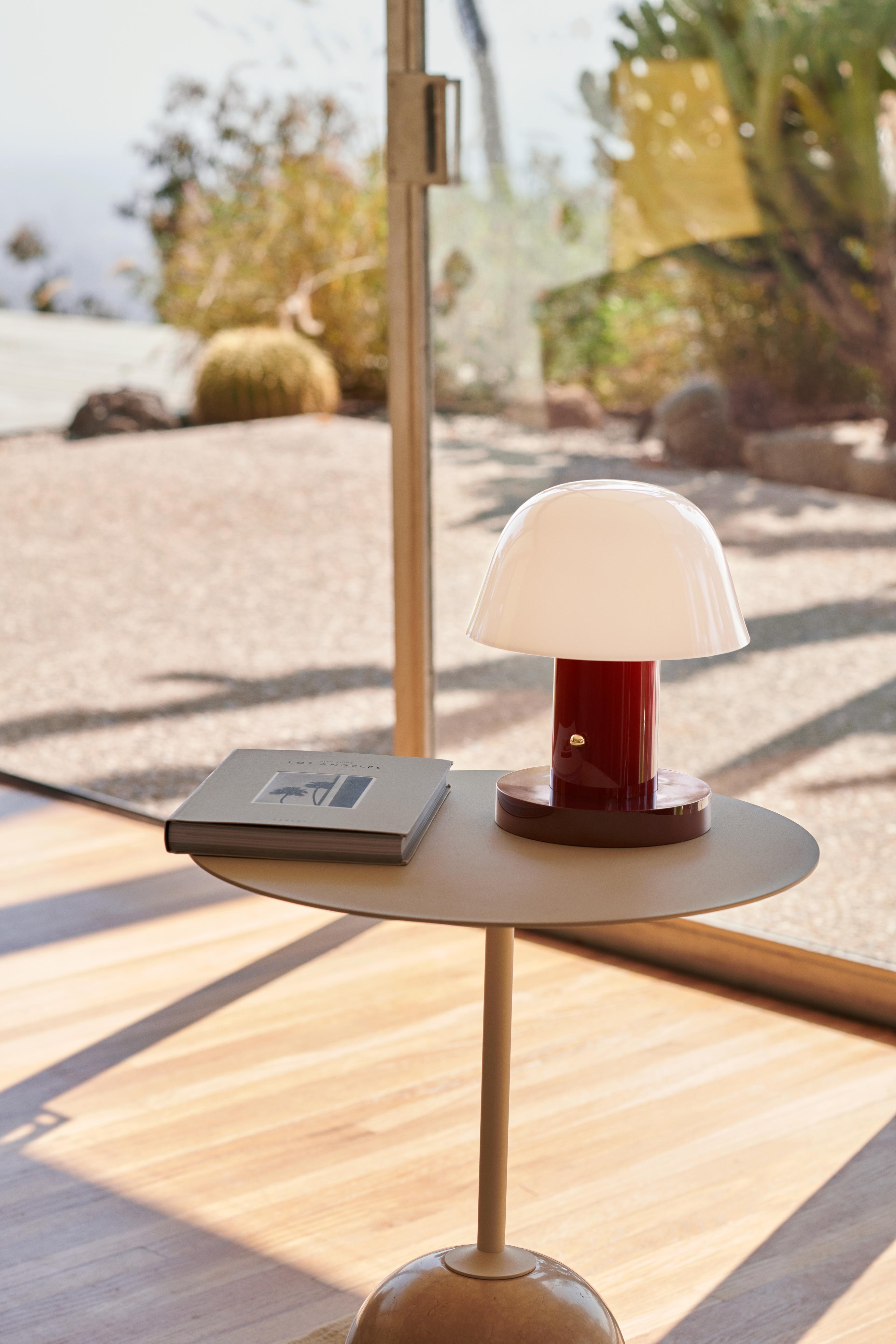 Tragbare Lampe SETAGO JH27 mit cremefarbenem Schirm und dunkelrotem Fuß.