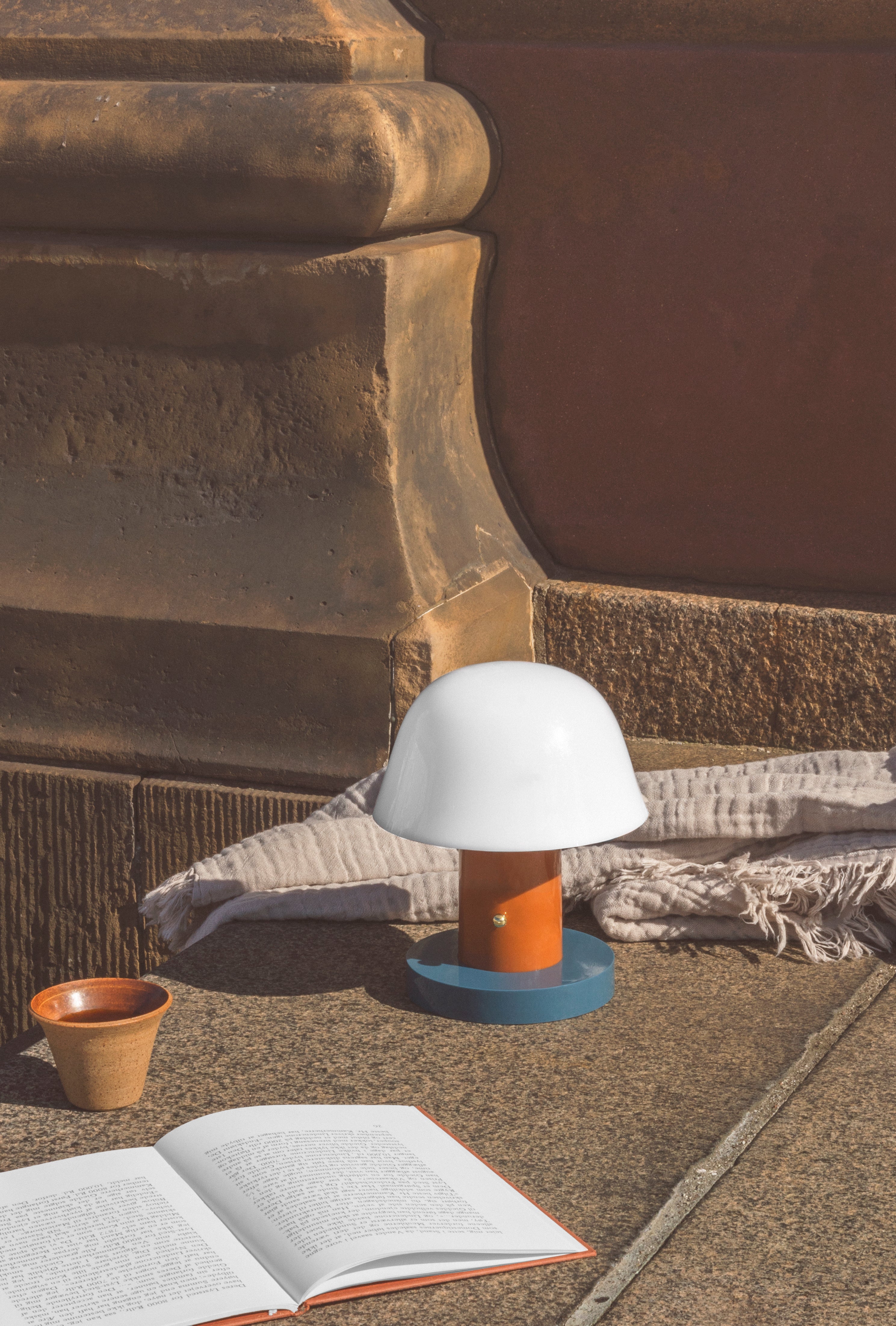 Tragbare Lampe SETAGO JH27 mit cremefarbenem Schirm und orange-blauem Fuß.